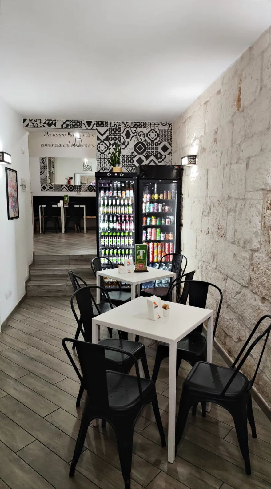 La sala con il muro in pietra, i tavoli bianchi e, in fondo, la parete di cementine